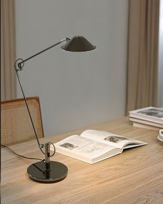 a desk lamp sitting on top of a wooden table next to an open book and coffee cup