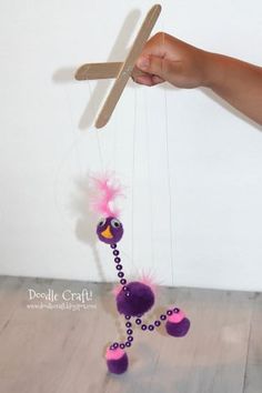 a person holding a wooden stick with a purple bird on it's string and beads