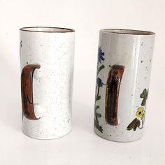 two coffee mugs with designs on them sitting side by side, one has a handle