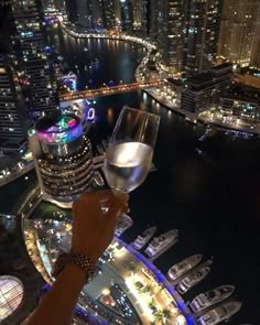 a person holding up a wine glass in front of a cityscape at night