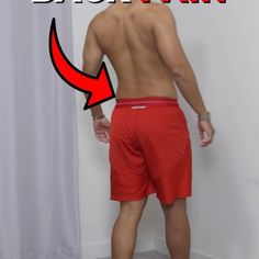 a man with no shirt standing in front of a white wall and wearing red shorts