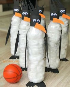 three penguins made out of plastic bottles sitting next to a basketball