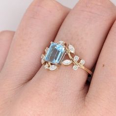 a woman's hand with a ring on it that has an aqua blue and white stone surrounded by leaves