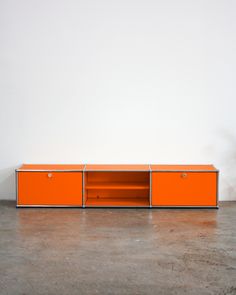 an orange sideboard with two doors and three drawers on the bottom, in front of a white wall