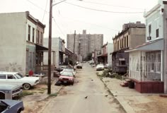 an old city street with cars parked on the side and buildings in the back ground