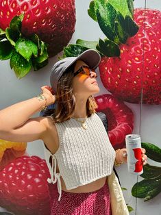 a woman standing in front of a wall with strawberries on it and holding a cup