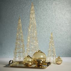 three small christmas trees and two ornaments on a tray with lights in the shape of domes