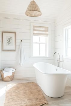 a white bath tub sitting under a window next to a rug on the floor in a bathroom