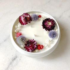 a white bowl filled with flowers on top of a marble countertop next to a candle