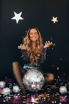 a woman sitting on top of a disco ball surrounded by confetti and stars