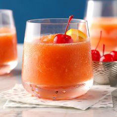 two glasses filled with orange juice and cherries on top of napkins next to each other