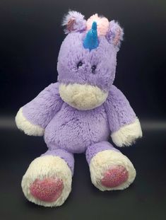 a purple stuffed animal with a pink heart on it's nose and tail sitting in front of a black background