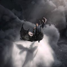 a man flying through the air on top of a black and white cloud filled sky