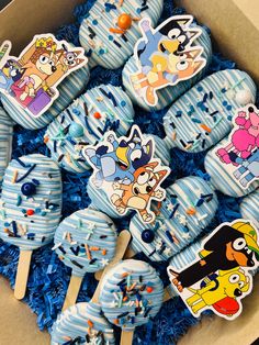 a box filled with cake pops covered in blue frosting and cartoon characters on them