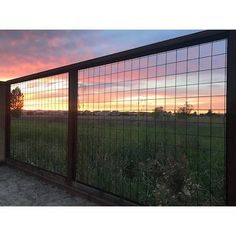 the sun is setting over an open field behind a fenced in area with tall grass