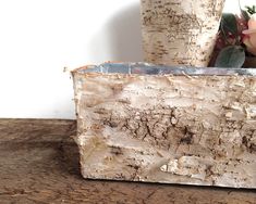 a close up of a vase with flowers in it on a wooden table next to a tree trunk