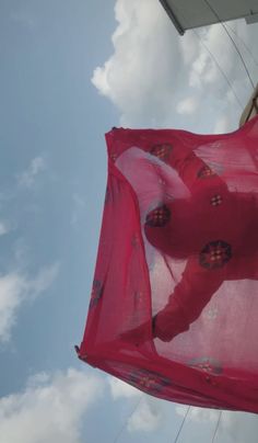 a red scarf hanging from the side of a building with clouds in the sky behind it