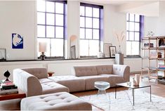 a living room filled with lots of furniture next to two large windows and a book shelf