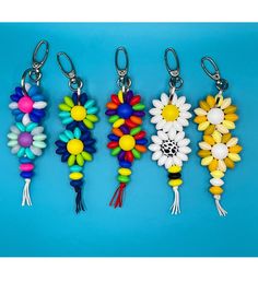 four key chains with flowers and beads hanging from them on a blue background in the shape of sunflowers