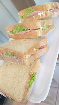 three sandwiches are stacked on top of each other in plastic wrappers and being held by someone's hand