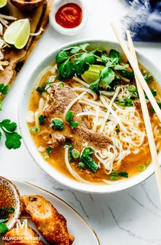 a bowl of soup with meat, noodles and vegetables on a table next to chopsticks