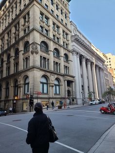 a woman is walking down the street in front of an old building with columns on it