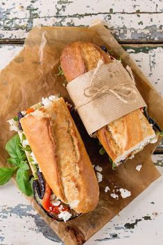 two sub sandwiches with lettuce and tomato on brown paper wrapper next to each other