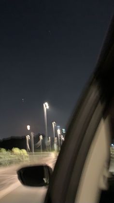 a car driving down the road at night time with street lights in the background and an airplane flying overhead