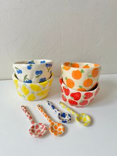 four bowls and three spoons are sitting on a white counter top, each with different designs