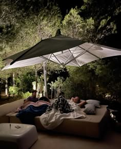 two people are laying under an umbrella on a bed in the middle of some trees