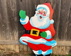 a santa clause standing in front of a wooden fence with his hand up to the side