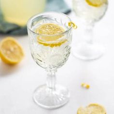 two glasses filled with lemonade sitting on top of a white tablecloth next to sliced lemons