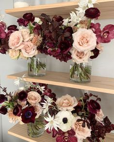 three glass vases filled with flowers on top of wooden shelves