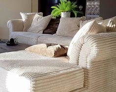 a white couch with pillows on it in front of a wall and a plant behind it