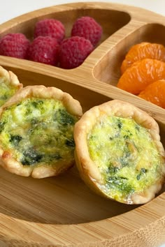 three small pies are on a wooden tray with raspberries and oranges