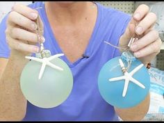 a woman is holding two glass ornaments in front of her face, both with starfish on them