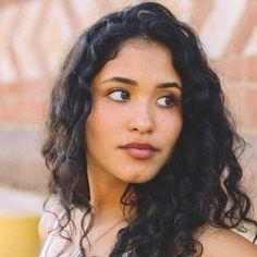 a close up of a person with long curly hair and a brick wall in the background