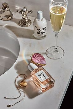 a bottle of perfume sitting next to a glass of wine on a sink counter top