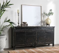 a room with a large mirror, plant and vases on the sideboard next to it