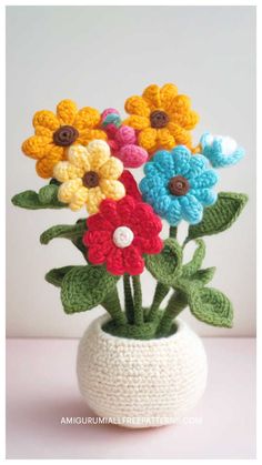 crocheted flowers in a white vase with green leaves on the top and bottom