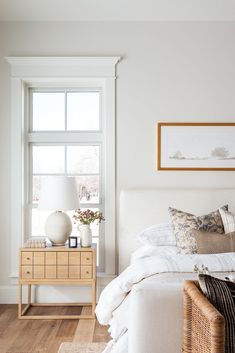 a bedroom with white walls and wood flooring has a wicker basket on the bed