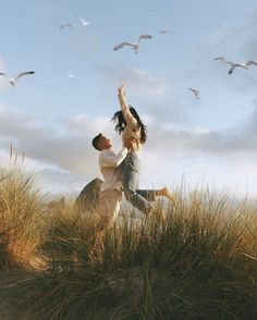 a man and woman standing on top of a grass covered field next to seagulls