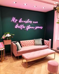 a pink couch sitting next to a green wall with neon writing on the wall above it