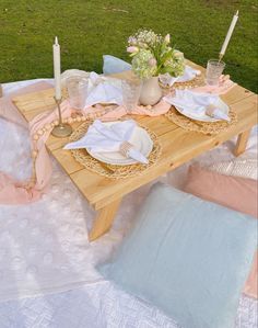 a wooden table topped with plates covered in pink and white cloths next to a field