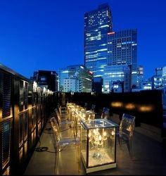 an outdoor dining area in front of a city skyline at night with lights on the tables