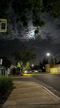 an empty street at night with the moon in the sky and trees on either side