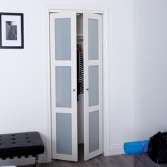 a white closet with glass doors and a bench in the corner next to it on a hardwood floor