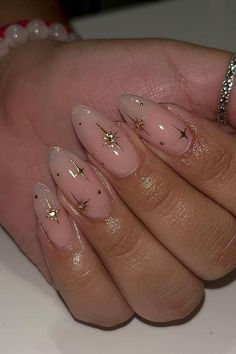 Elegant almond-shaped nails with a translucent pink base, subtly enhanced with tiny gold star accents and specks of gold glitter creating a minimalistic yet chic look. The design is understated and perfect for adding a touch of sparkle to everyday style. Simply charming! ✨  // Photo Credit: Instagram @nailsbykarenm_ Almond Nails With Sparkle Design, Chrome Nails Designs Stars, Gold Star Almond Nails, Prom Nails Inspo Almond, Almond Shaped Star Nails, Clear Nails With Gold Stars, Hold Accent Nails, Charm Nails Almond