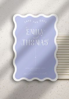 save the date card with blue background and white lettering on it, in front of a wall