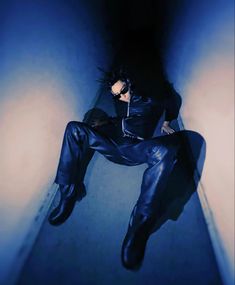 a man sitting on the floor with his legs up in the air and wearing black leather pants